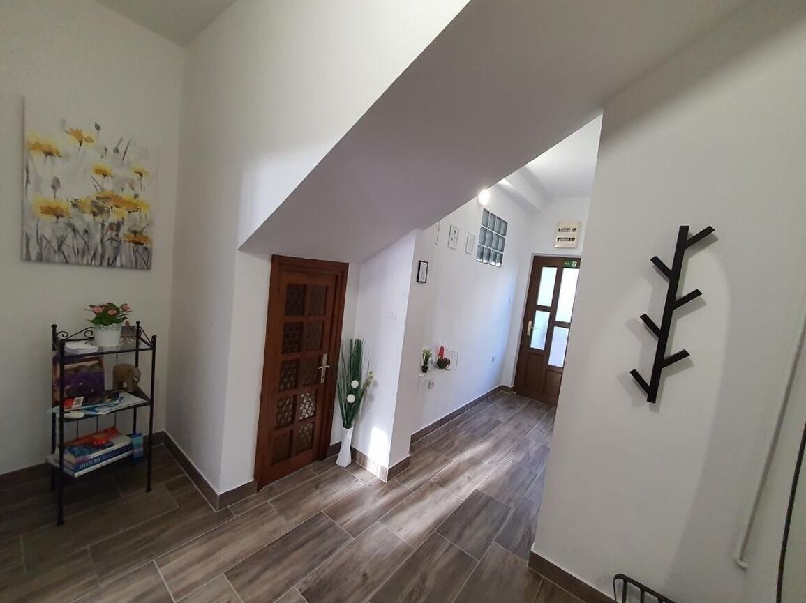 Um corredor com porta de madeira, um porta-roupas preto fixado na parede e uma pintura de flores na parede.