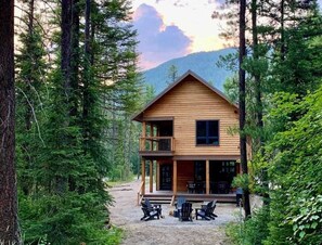 A wooden cabin with a balcony, surrounded by trees and a mountain in the background.