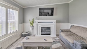 Een woonkamer met een open haard, een bank, een salontafel en een aan de muur bevestigde televisie.