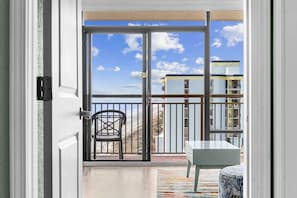 A balcony with a chair and a table, a view of buildings, and a clear sky. - Beach View Retreat,KING,Pools,M149 (Myrtle Beach)