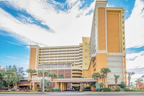 A multi-story hotel with a central atrium, a covered entrance, and palm trees in the foreground. - Beach View Retreat,KING,Pools,M149 (Myrtle Beach)