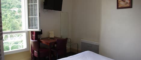 A hotel room with a bed, a desk with a chair, a television on the wall, and a window with curtains.