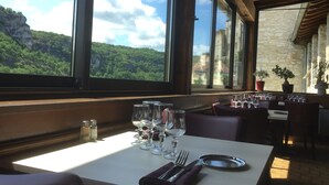 Un restaurant avec une table dressée pour deux personnes, de grandes fenêtres offrant une vue sur un paysage montagneux.