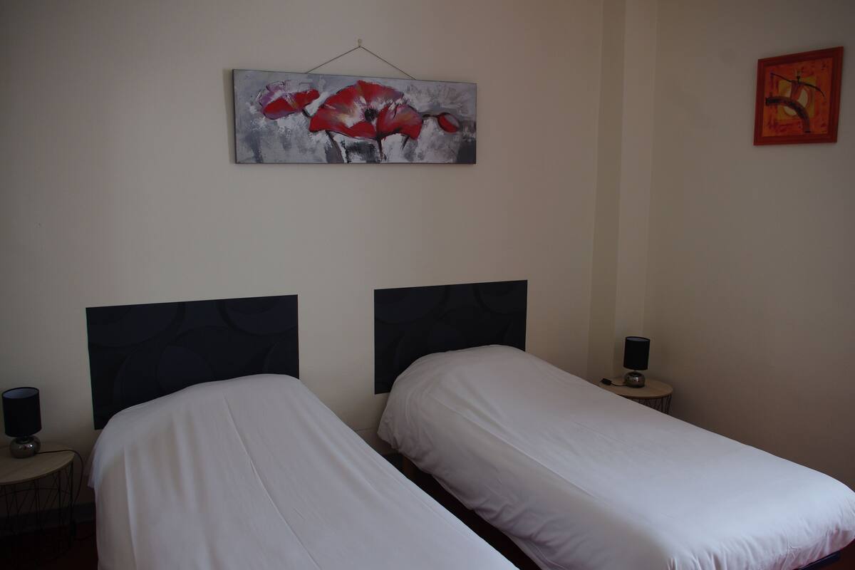 Una habitación de hotel con dos camas, un cuadro de flores rojas en la pared y una mesita con una lámpara.