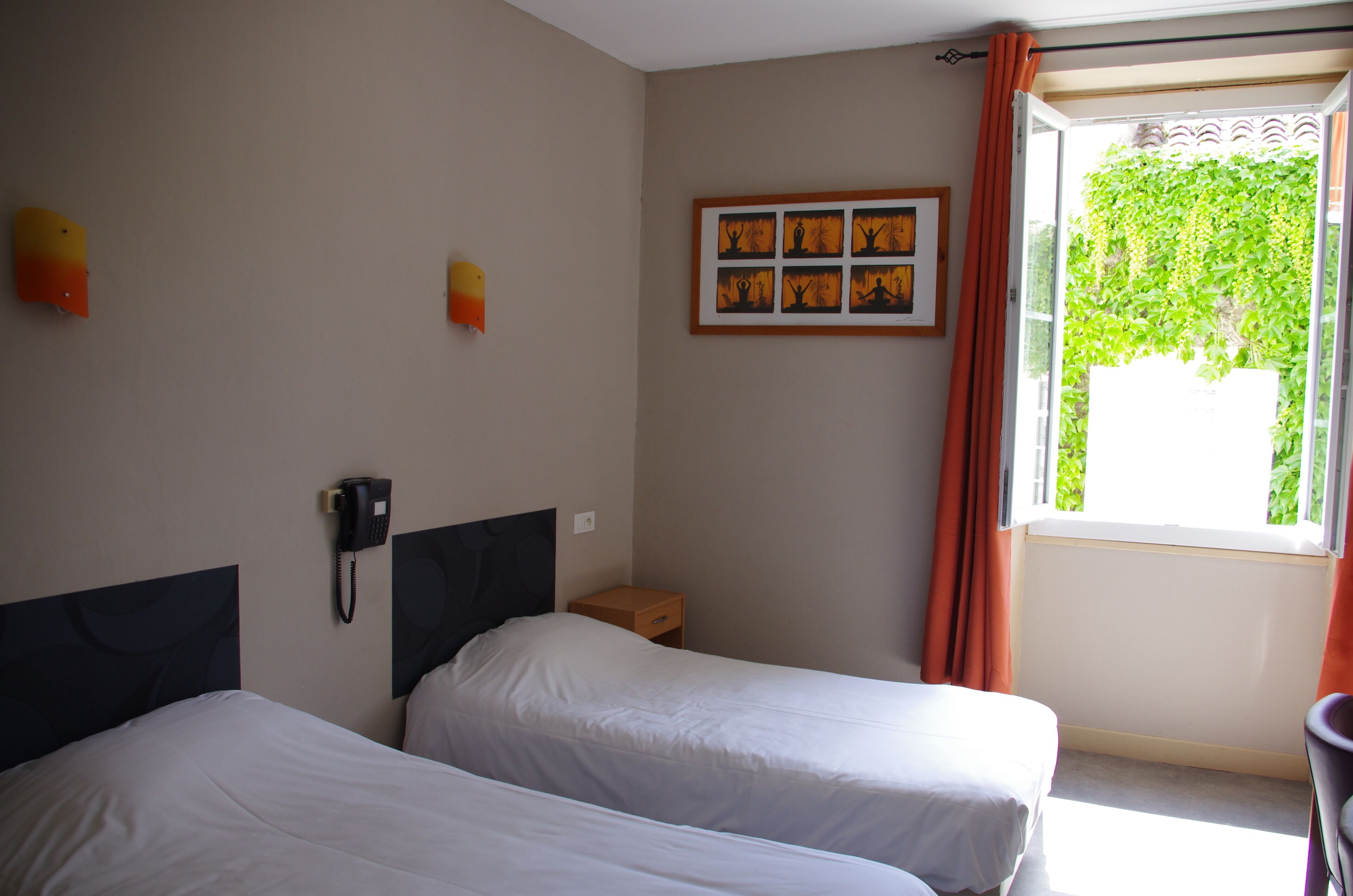 Habitación de hotel con dos camas, un teléfono en la mesita de noche, una pequeña mesita de madera y una ventana con cortinas.