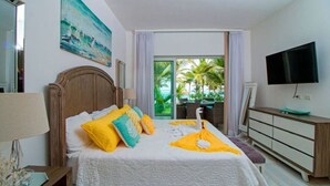 Ein Hotelzimmer mit Bett, Fernseher, Kommode und einem Balkon mit Blick auf Palmen.