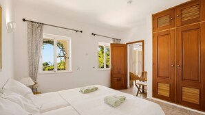 A bedroom with two beds, a wooden wardrobe, and a view of greenery outside.