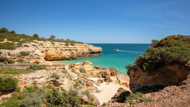 A coastal landscape with rocky cliffs, a sandy beach, and a clear blue sky.