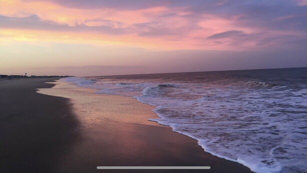 Una spiaggia con un litorale curvo e onde che si infrangono sulla riva.