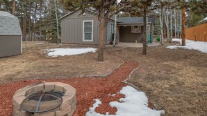Un jardin avec un foyer extérieur, un abri de jardin et une clôture en bois.