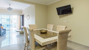 Un coin repas comprenant une table rectangulaire, six chaises en osier, un élément décoratif mural et un téléviseur à écran plat fixé au mur.