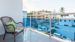 Un balcon avec un fauteuil en osier et une vue sur un quartier résidentiel comprenant de nombreux immeubles et des voitures garées.