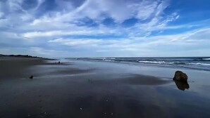 A beach with a large rock in the foreground and a cloudy sky. - Beach House (Corolla)