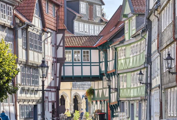 A narrow street with traditional half-timbered buildings, a covered passageway, and outdoor seating areas.