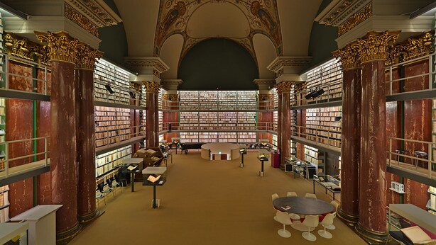 Eine prachtvolle Bibliothek mit hohen Decken, aufwendigen Säulen und umfangreichen Buchbeständen.