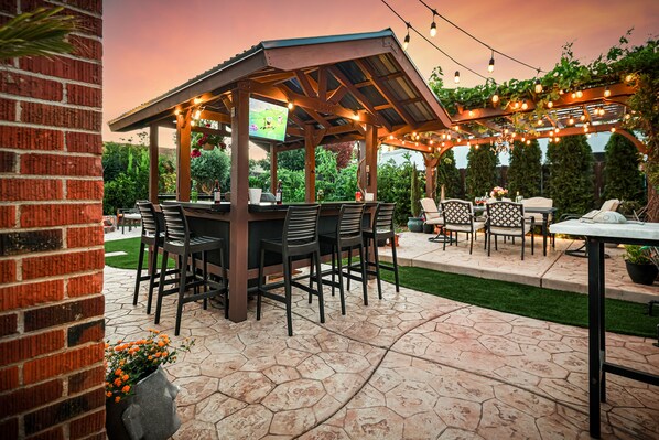 An outdoor patio with a covered seating area, stone flooring, and string lights.