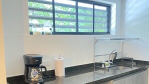 A modern kitchen with a black countertop, a coffee maker, a red appliance, and a window with blinds. - Hotel 14-04 (Cali)