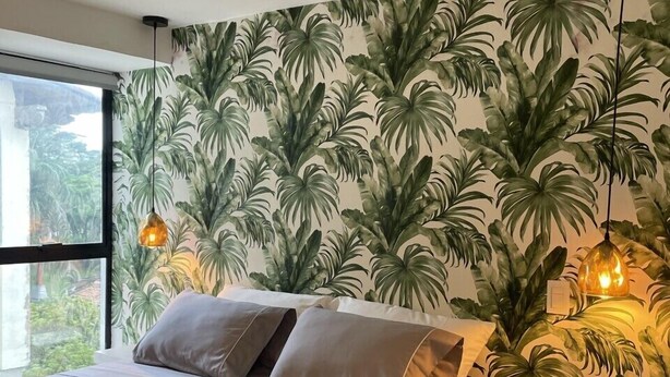 A modern bedroom with a bed, a nightstand, and a wall with a tropical leaf pattern. - Hotel 14-04 (Cali)