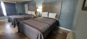 A hotel room with two beds, a nightstand, a lamp, and a window with curtains. - HOTEL BLUE (DeLand)