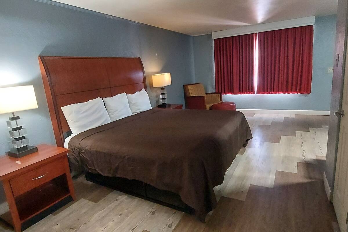 A bedroom with a wooden bed, two bedside tables with lamps, a red curtain, and a wooden floor.