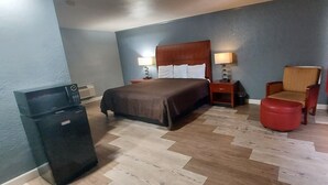 A hotel room with a bed, bedside tables, a chair, a red ottoman, and a refrigerator. - HOTEL BLUE (DeLand)