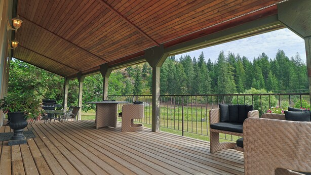 Una terraza cubierta al aire libre con piso de madera, una parrilla, mobiliario exterior y vistas a un área boscosa.