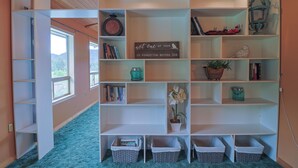 Una habitación con una amplia estantería blanca, un ventanal con vistas y una puerta que da a otra estancia.