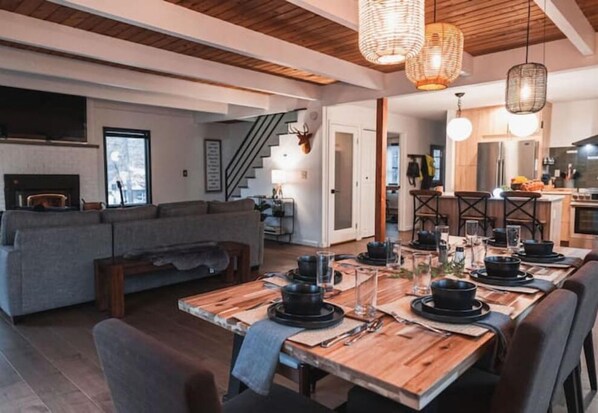 A modern dining area with a wooden table set for a meal, a grey sofa in the background, and a staircase leading to another level.