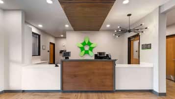 A reception area with a wooden reception desk, a green logo on the wall, and a modern ceiling design.
