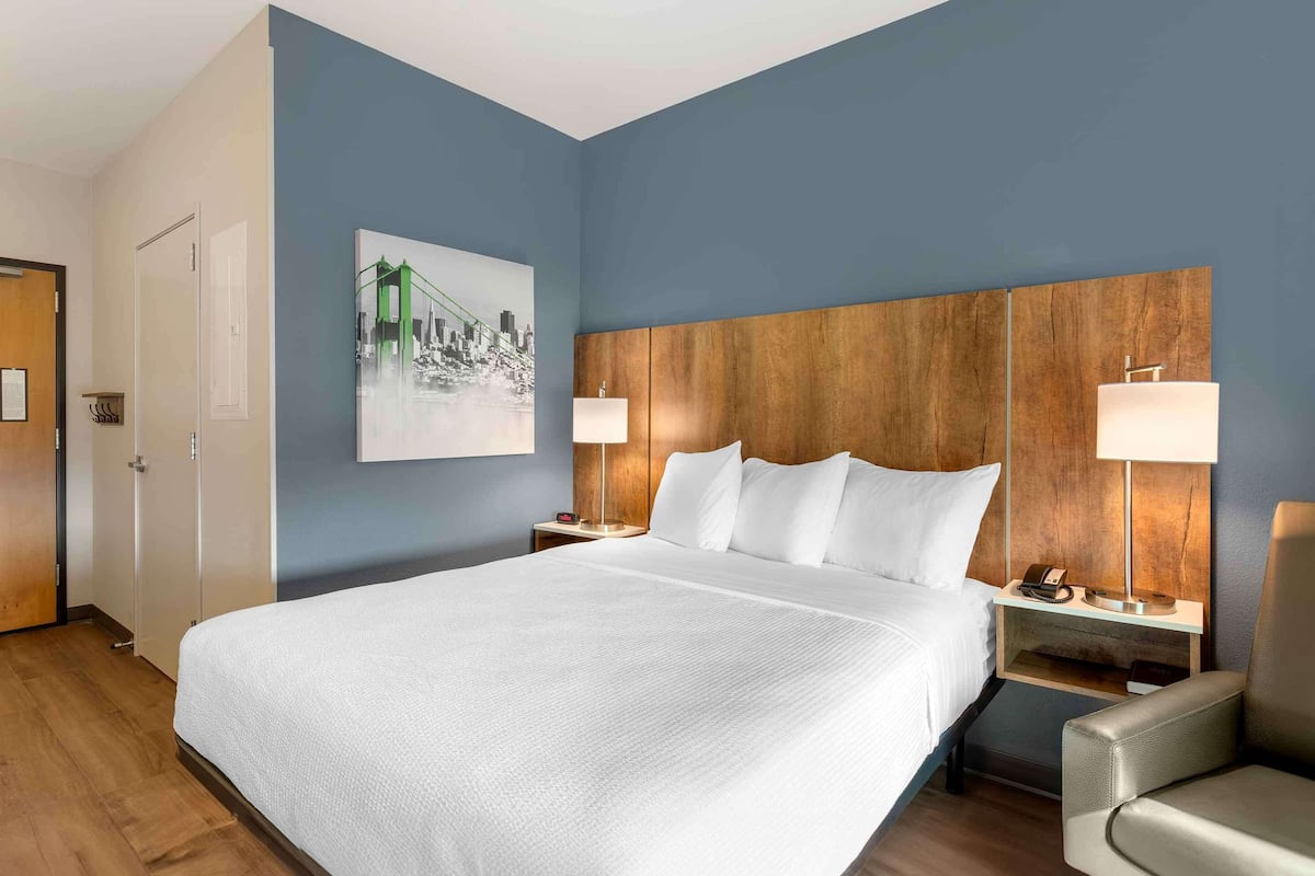 A hotel room with a large bed, two bedside tables with lamps, a chair, and a painting on the wall.