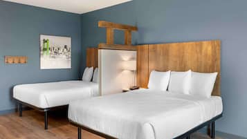 Habitación de hotel con dos camas individuales, un cabecero de madera, una mesita de noche con lámpara y una pintura de paisaje urbano en la pared.