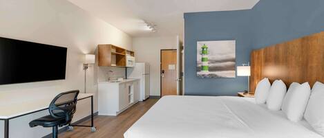 Een moderne hotelkamer met een groot bed, een bureau met stoel, een kitchenette en een schilderij van een vuurtoren.