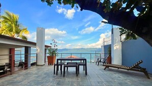 Une terrasse extérieure avec une table et des chaises, un pot de fleurs et une vue sur la mer.