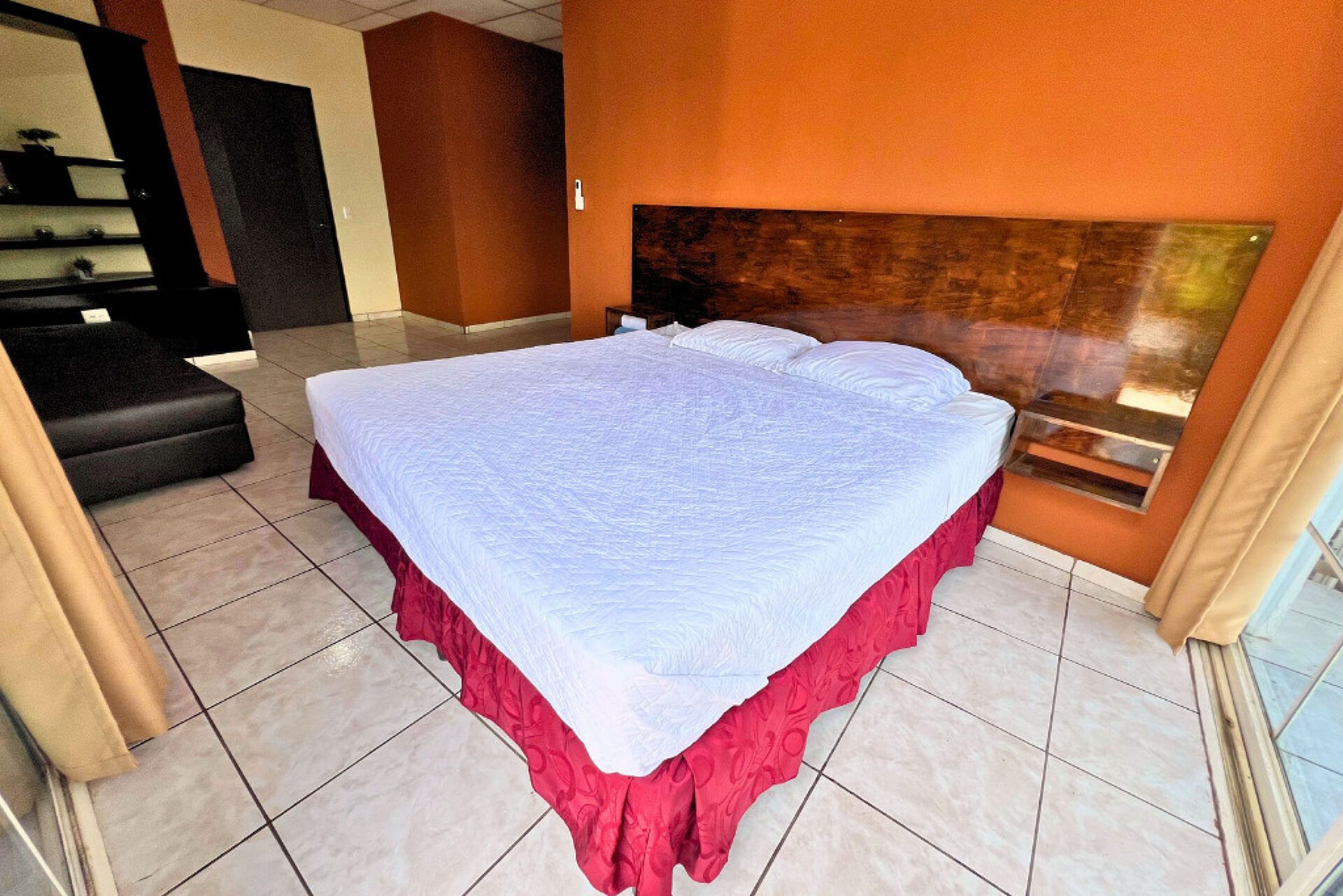 A hotel room with a large bed, a wooden headboard, and a view of the outdoors.