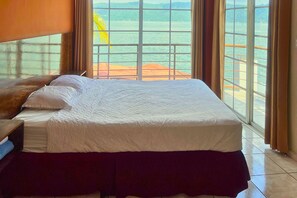 A hotel room with a bed, a nightstand, and a view of the sea through large windows.