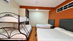 Une chambre avec des lits superposés et un lit simple, une fenêtre et une bouche d’aération au plafond.