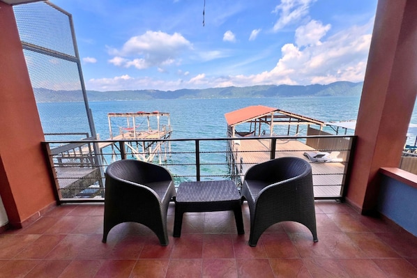A balcony with two wicker chairs, a view of the sea, and a wooden deck with a red roof.