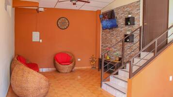 Quarto com escada, ventilador de teto, relógio e televisão na parede.