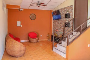 A room with a staircase, a ceiling fan, a clock, and a wall-mounted television.