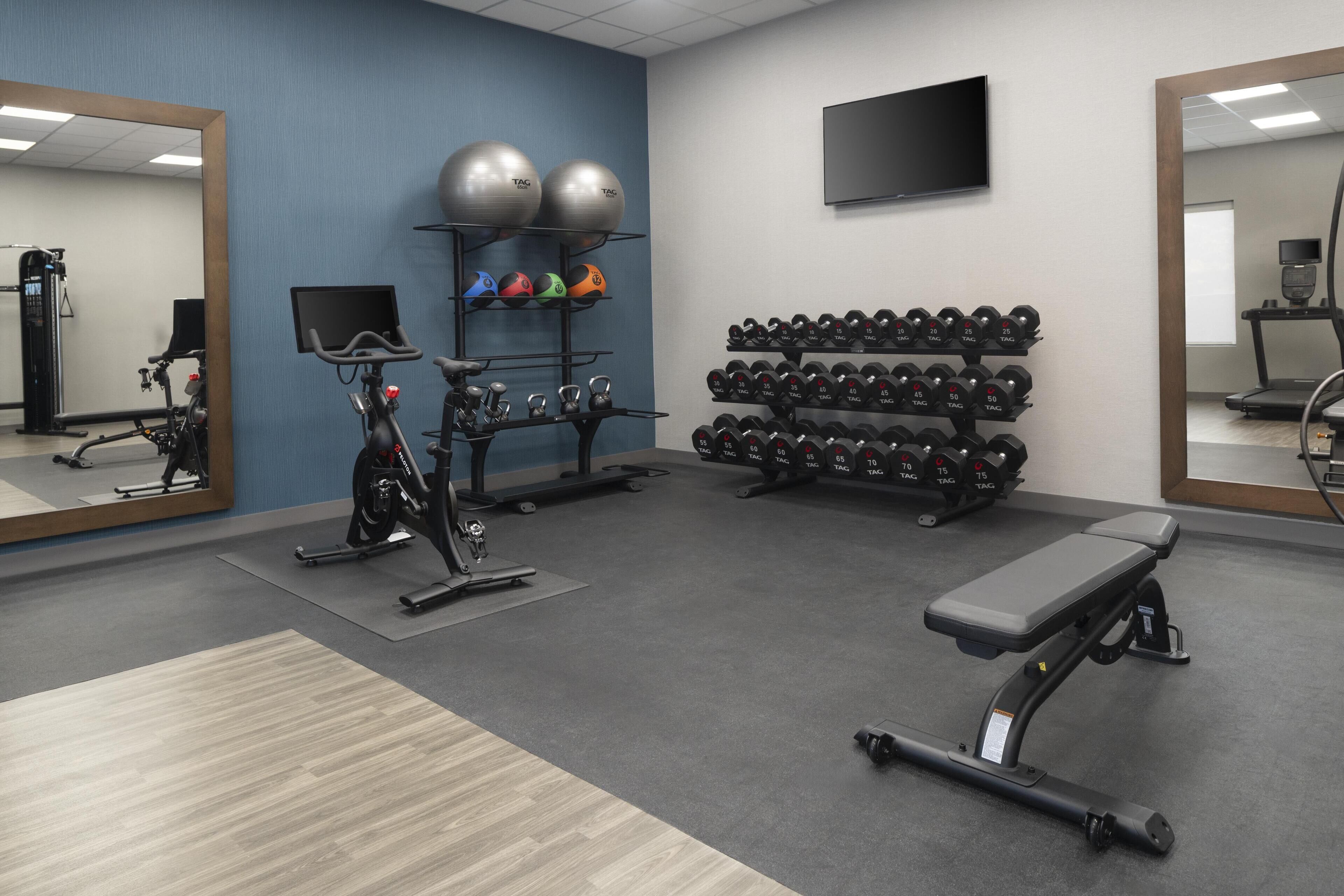 Un gimnasio con equipo de ejercicio, un televisor en la pared y un espejo.