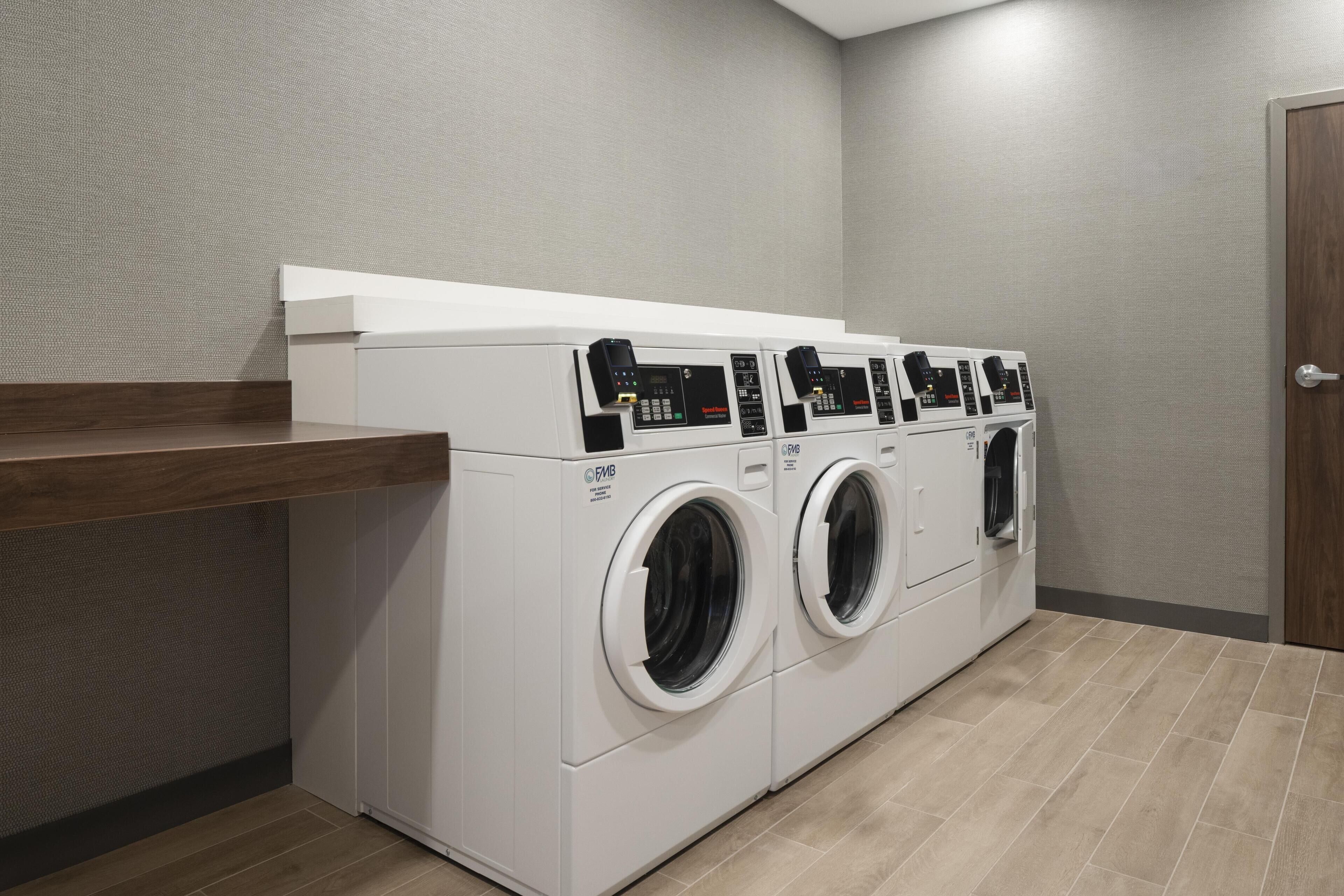 A laundry area with three front-loading washing machines and a wooden counter.