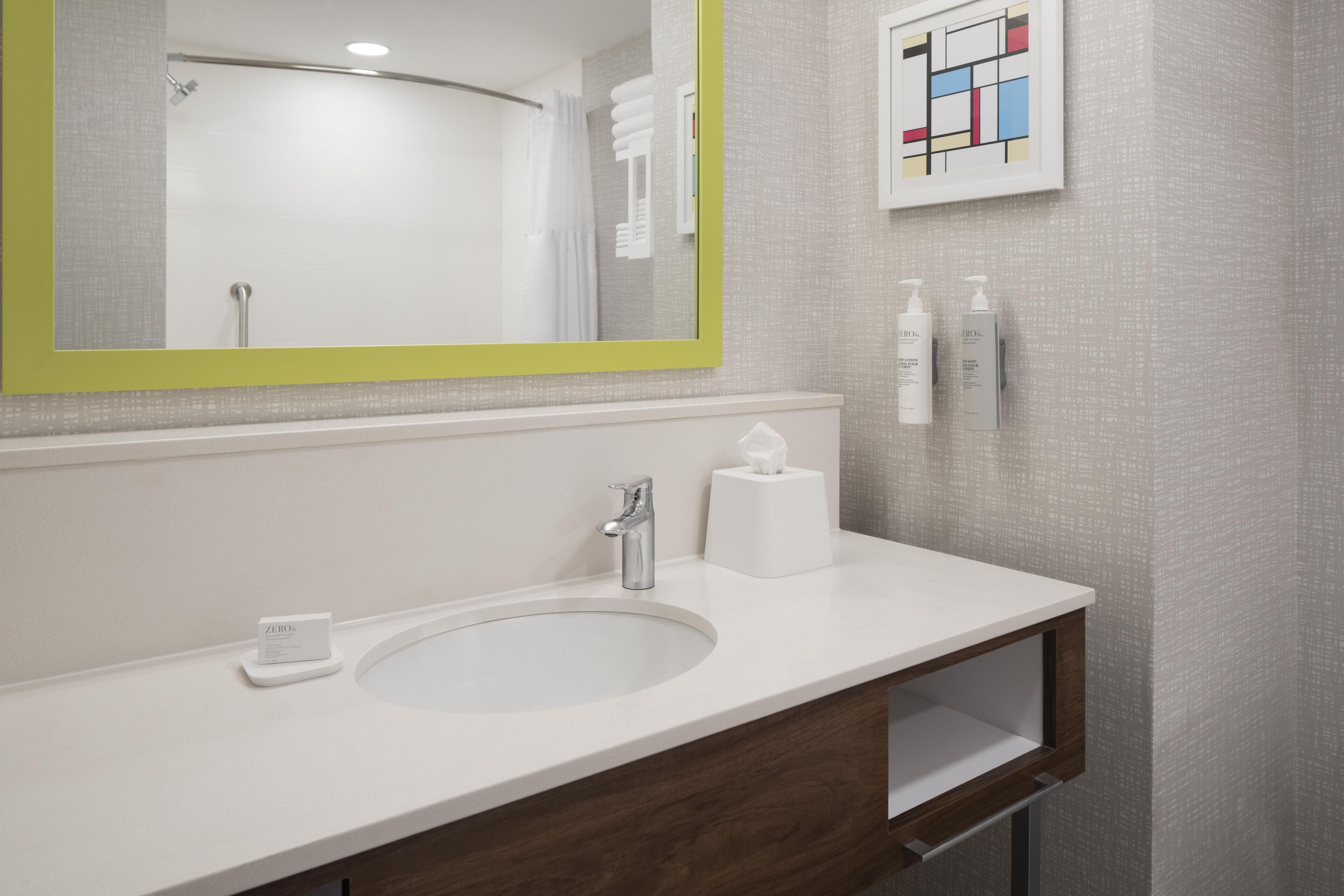 Une salle de bain moderne avec un lavabo blanc, un miroir à cadre vert et des articles de toilette accrochés au mur.
