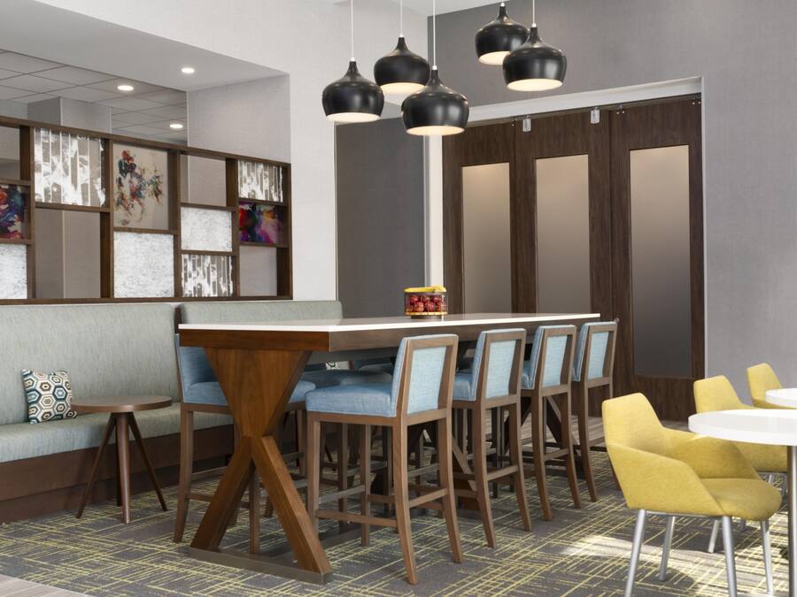 Un espace bar moderne avec un comptoir en bois, des tabourets de bar bleus rembourrés et des luminaires suspendus noirs.