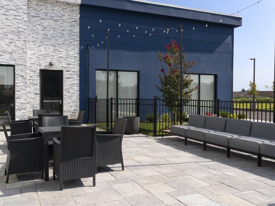 An outdoor patio with wicker furniture, a grey sofa, and a modern building with large windows and a blue facade.