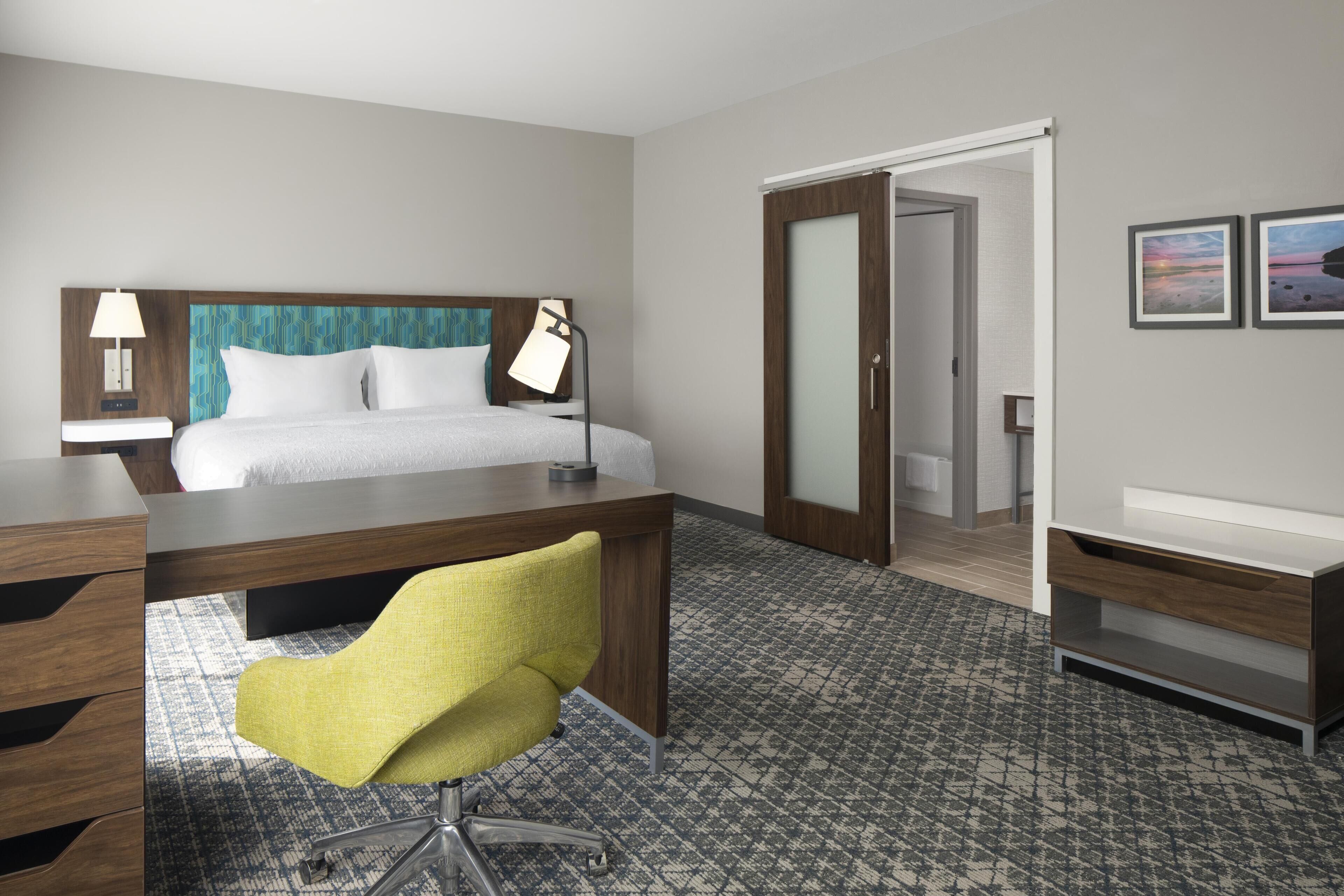 A hotel room with a bed, desk, chair, and a bathroom visible through an open door.