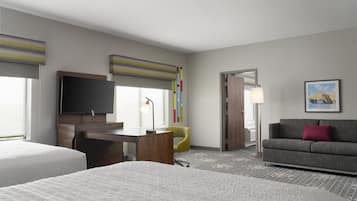 A hotel room with two beds, a desk, a television, a sofa, and a colorful artwork on the wall.
