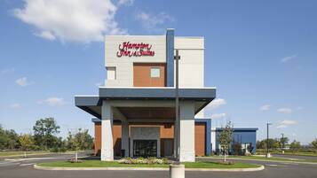 A modern Hampton Inn & Suites with a prominent sign, a central entrance, and landscaped surroundings.