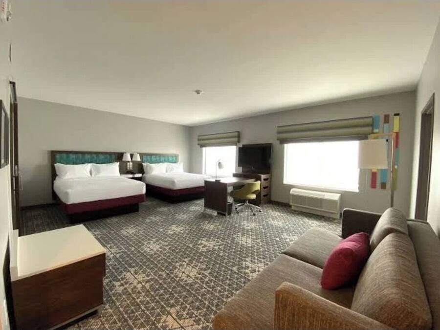 A hotel room with two beds, a desk, a chair, a sofa, and a TV.