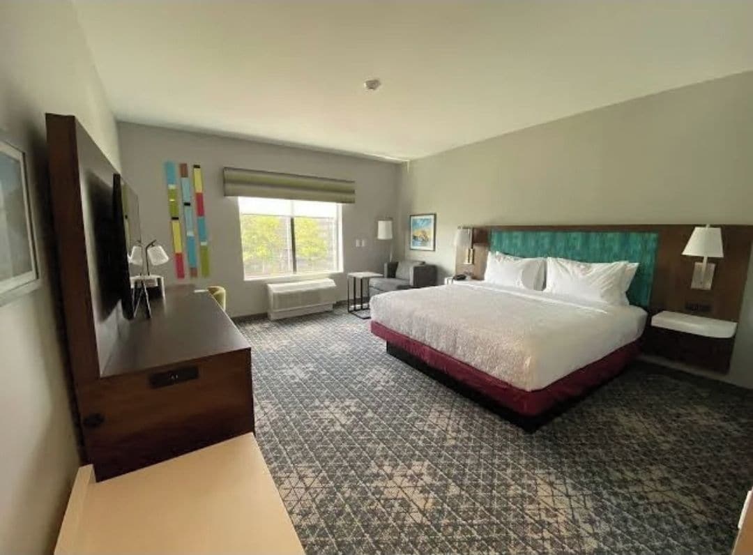 A hotel room with a large bed, a desk, a chair, a TV, and a window.