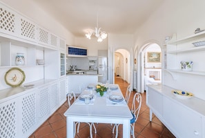 Una cocina amplia con muebles blancos, una mesa de comedor para cuatro personas y una isla central.